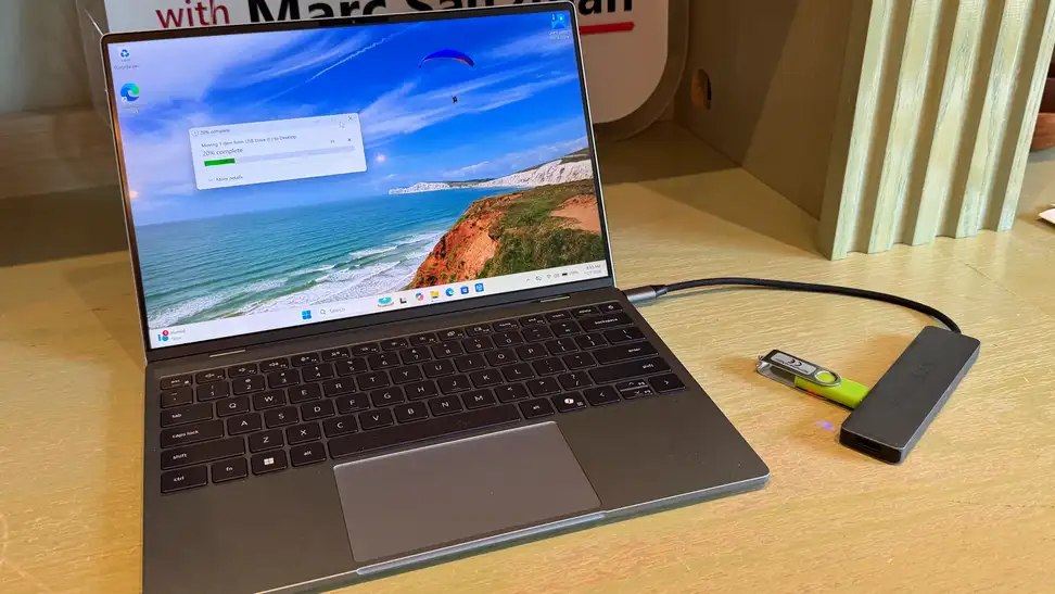 Dell XPS 13 sitting on a wooden surface with a USB adapter and flash drive plugged into the right side.