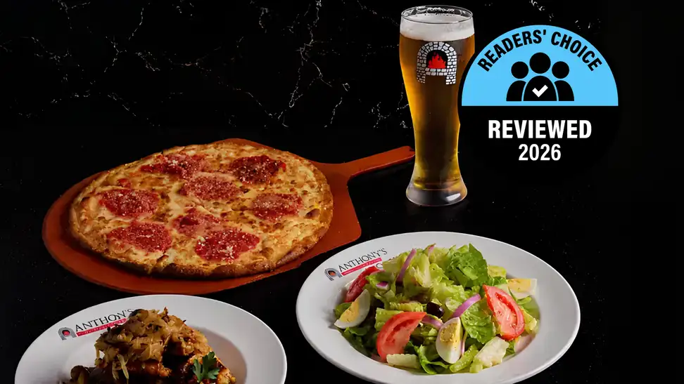 An Anthony's Coal Fired Pizza spread on a dark marble surface featuring a pepperoni pizza on a wooden peel, a side of roasted vegetables, a garden salad, and a branded pint of beer, overlaid with a Readers' Choice Reviewed 2026 badge.