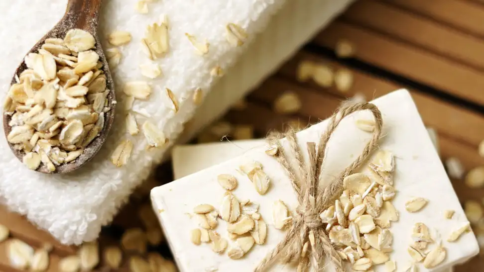 Spoon full of oats next to a bar of soap sprinkled with oatmeal