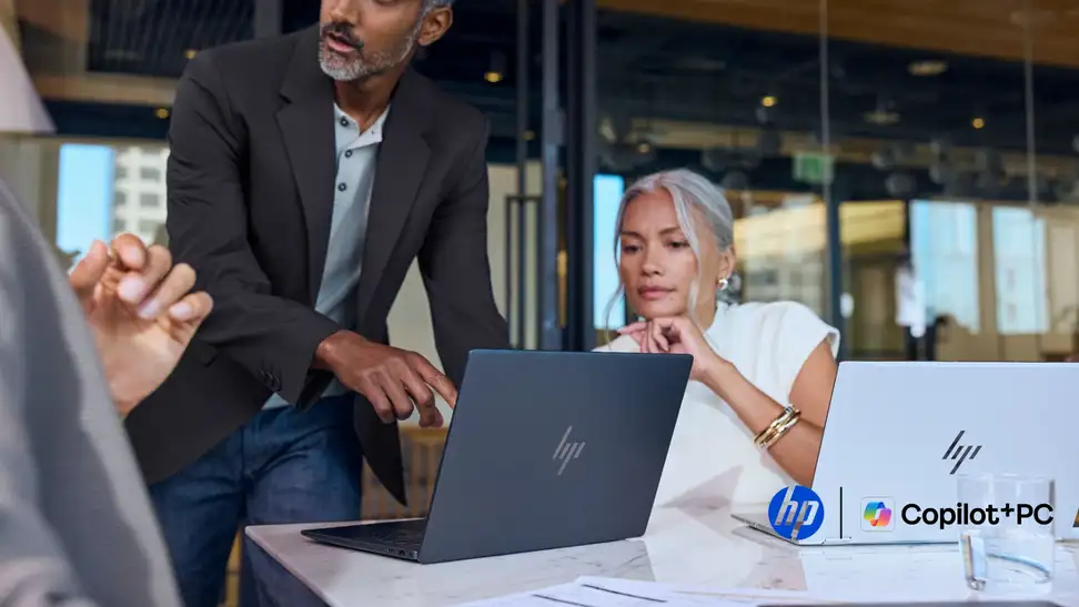 Man leaning over an HP in an office next to a woman who also has an HP EliteBook X
