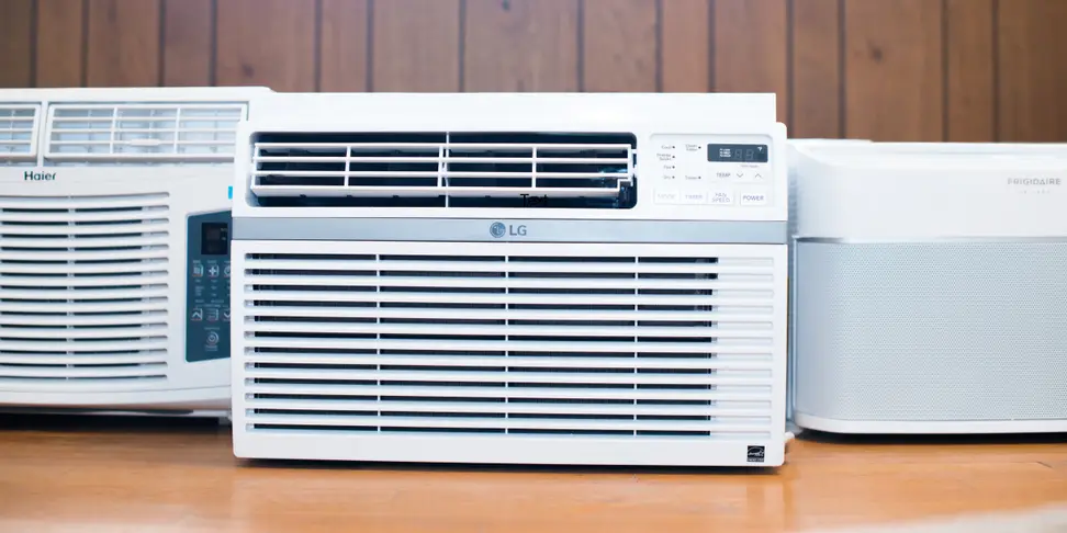 Three of the best window air conditioners are displayed on a wooden countertop, all are white.