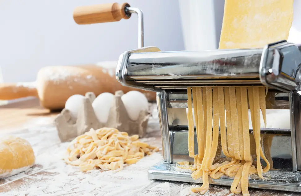 Eggs and freshly made noodles sit on a counter next to a hand-crank pasta maker.