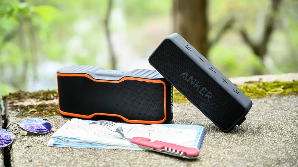 A couple great Bluetooth speakers sit outdoors against a lovely backdrop of green trees