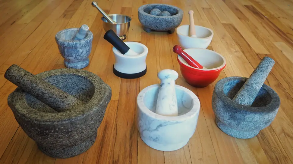Nine stone, ceramic and marble mortars and pestles are lined up on a table