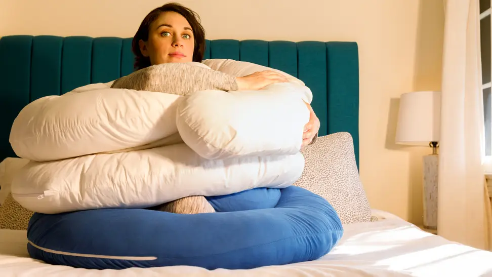 Writer Steph Garcia sits on a bed surrounding by pregnancy pillows.