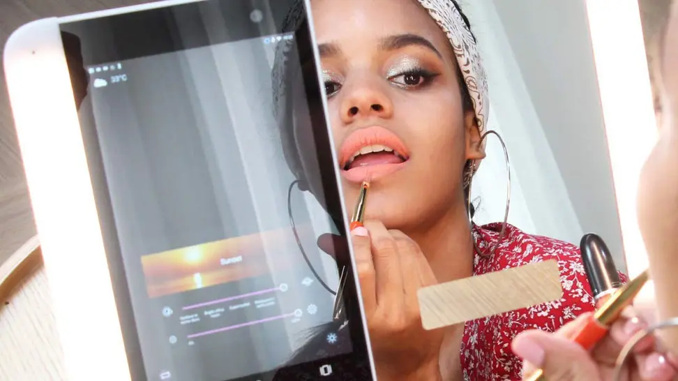 HiMirror Slide smart lighted mirror open with woman's reflection in mirror and tablet showing light settings on the left