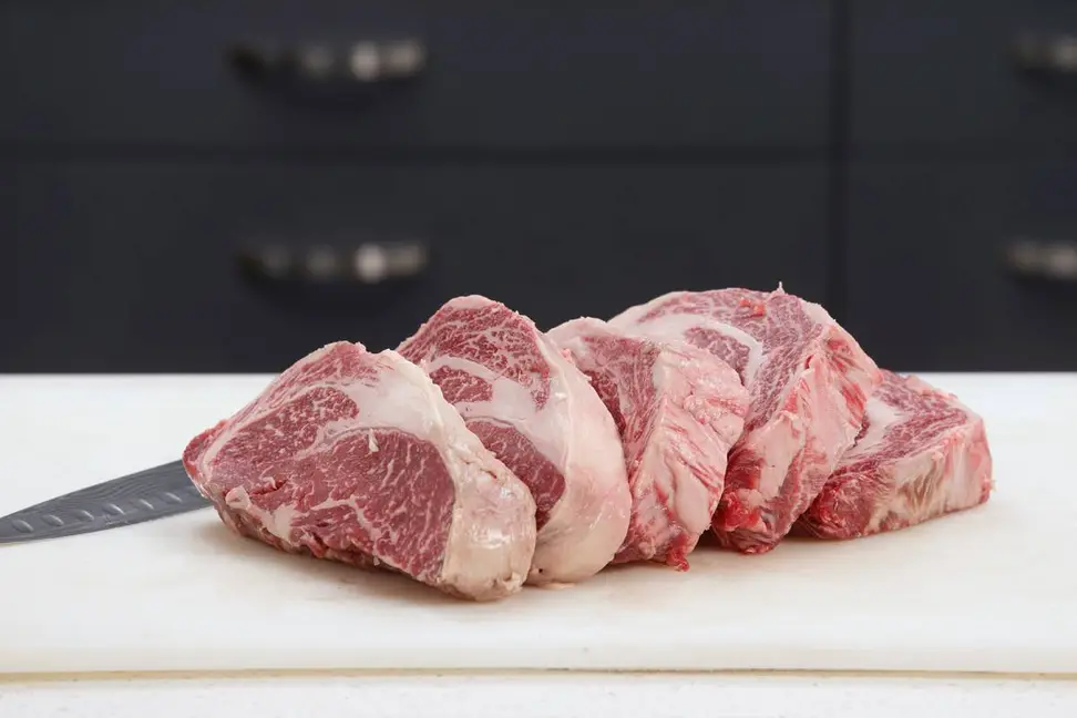 On a white cutting board, there are five thick slices of uncooked American Wagyu beef, produced by Snake River Farms.