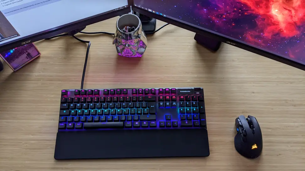 A steelseries Apex pro, one of the best gaming keyboards on the market, on a desk between two monitors tilted inward