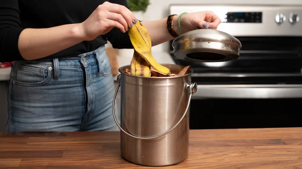 Woman putting banana peel into stainless steel countertop compost bin.