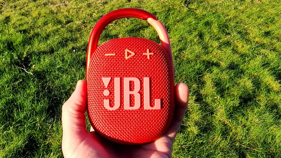 JBL Clip 4 red Bluetooth speaker in-hand before green grass