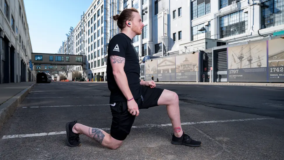 A person wearing earbuds takes a moment to stretch in a city parking lot.