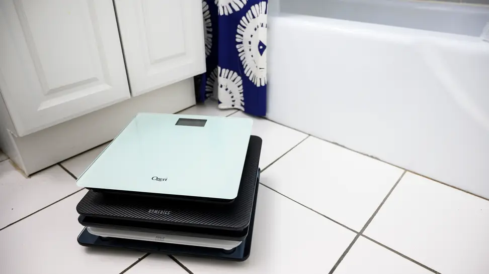 A stack of bathroom scales resting on a tile floor next to a tub in the bathroom