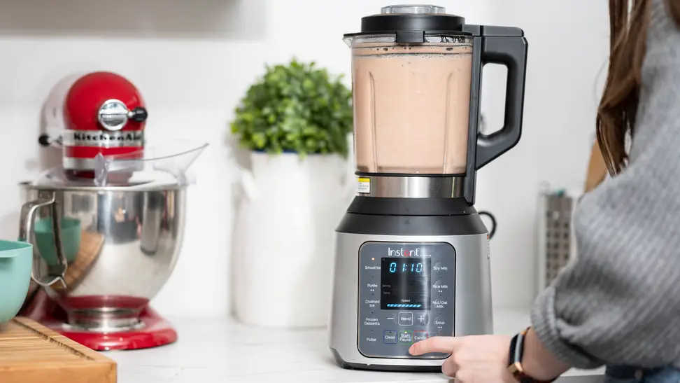 A person blends a smoothie in a blender on a countertop surrounded by other kitchen items.