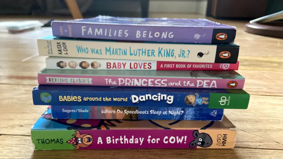 Stack of seven multi-colored children's books on a tan hard wood floor.