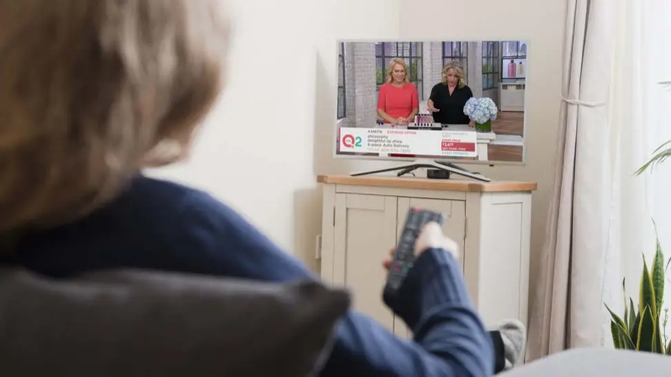 blonde person watching QVC channel on TV.