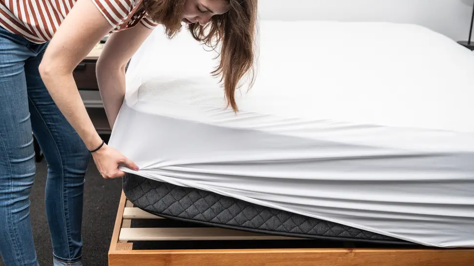 A person puts a mattress protector on a mattress
