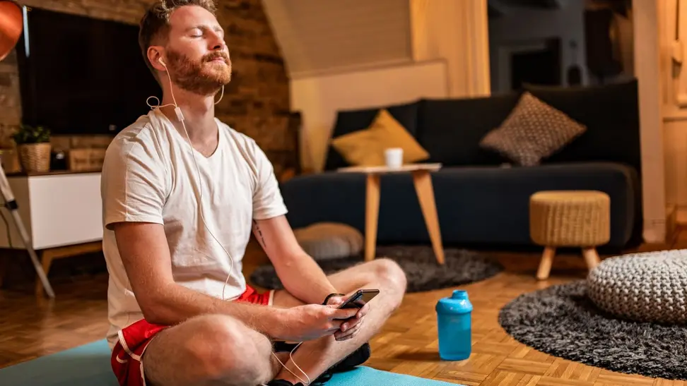 a person sits on a yoga mat holding their phone and listening to audio as though they're meditating