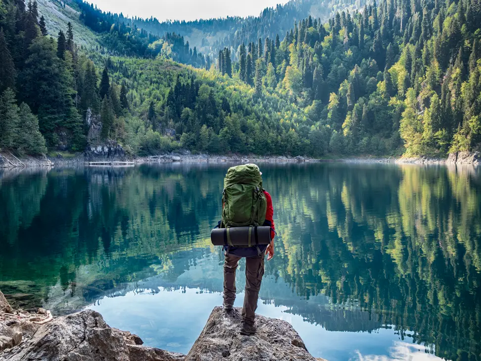 A hiker overlooks a beautiful body of water surrounded by hills and trees.