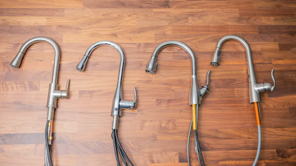 Four uninstalled kitchen faucets lay on their sides on a butcherblock counter