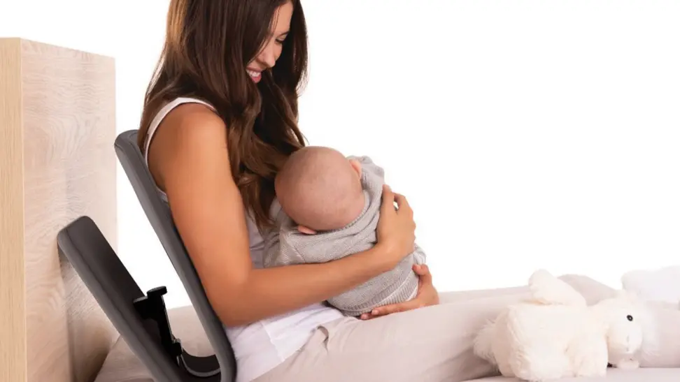 A mother smiles at her baby as they sit on a bed using the Ready Rocker.