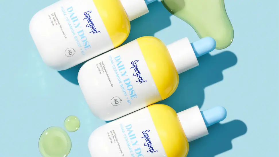 Three white, yellow, and blue colored bottles lay in a row with swatches of oil around them.