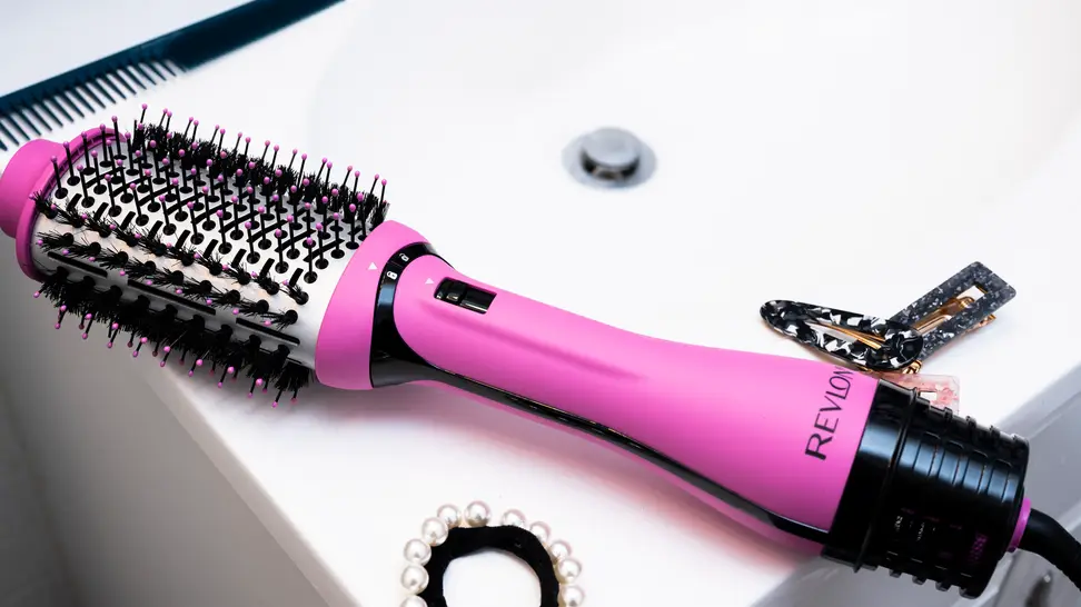 A hair dryer brush laying on the countertop of a sink with hair accessories around it.