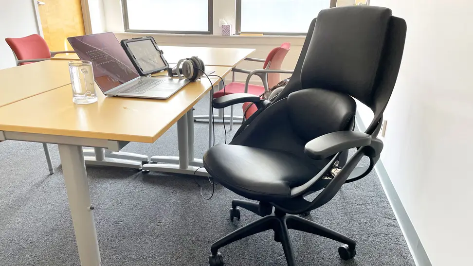 A downward view of the chair sitting at one of the conference room tables in our office. There's a laptop and iPad set up in front of it with headphones attached.