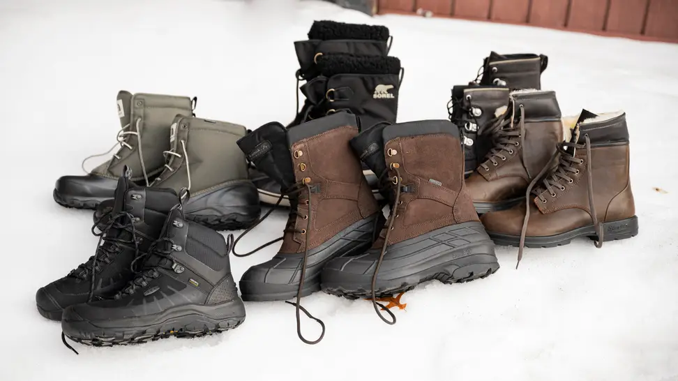 A wide selection of men's winter boots, sitting on a bank of snow.