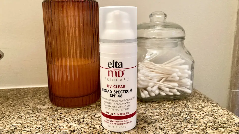 A bottle of sunscreen sitting on a granite sink countertop with a soap dispenser and container of cotton swabs behind it.