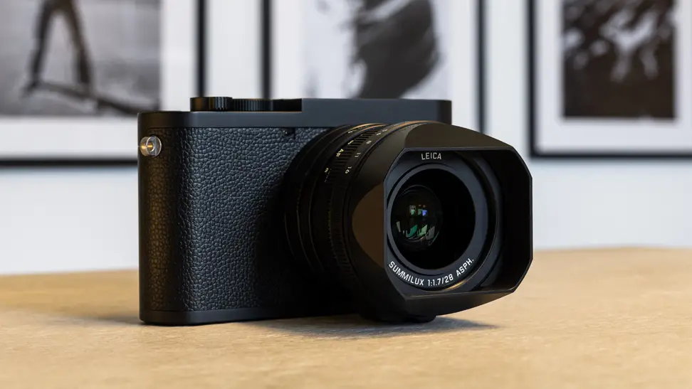 A Leica Q2 Monochrom camera sits on a wooden table in an art gallery.