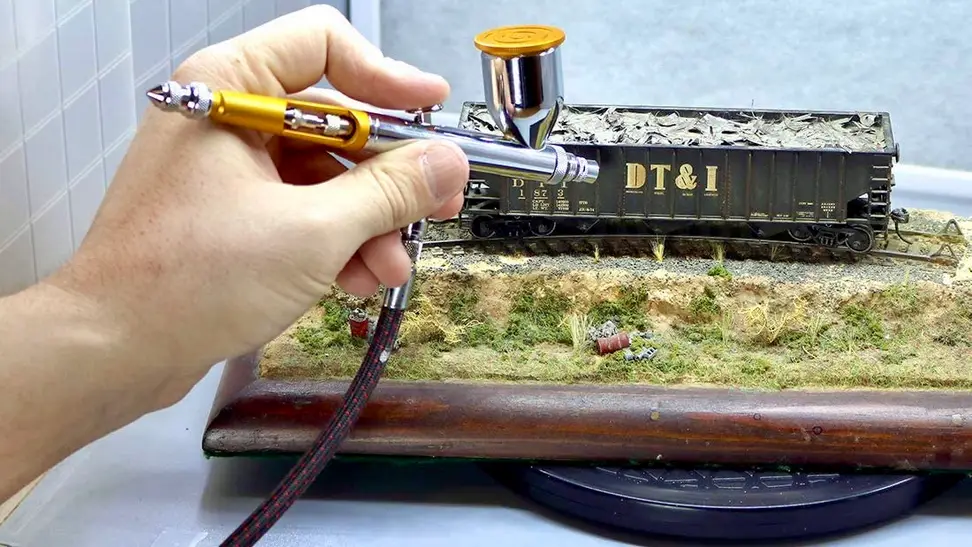 A person airbrushes text onto the side of a train model.