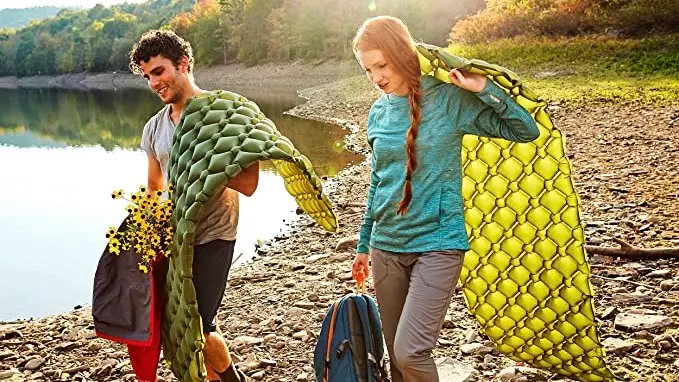 A couple carrying two Sleepingo camping sleeping pads outside while holding additional gear