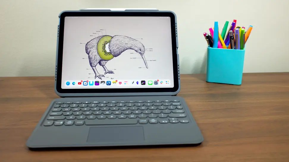A tablet with an attached keyboard on a wooden desk with an aqua blue pencil holder contains writing instruments in the background
