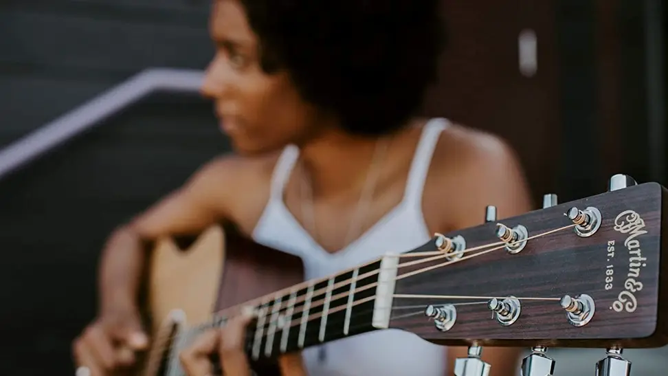 A woman playing her Martin acoustic guitar in a seated position.