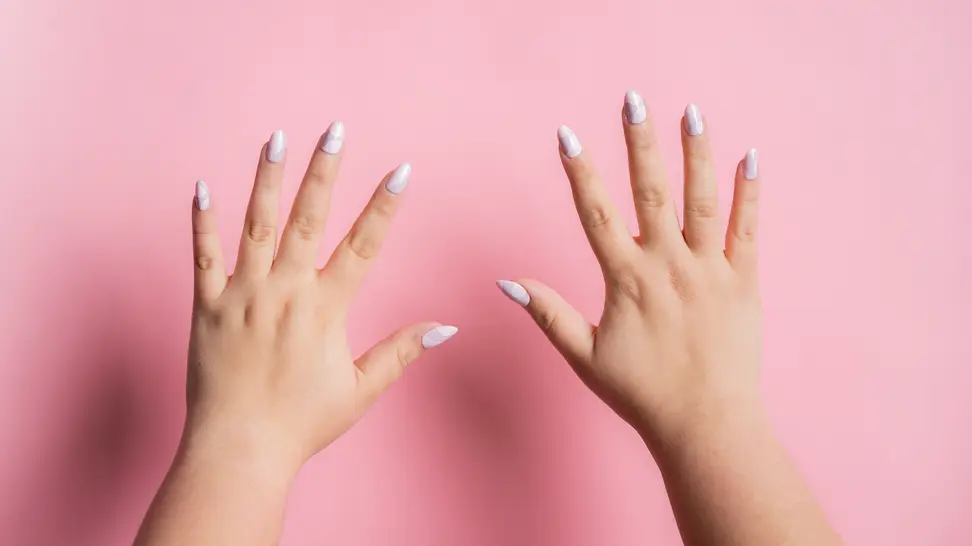 Two hands with press-on nails on them held up in front of a pink wall.
