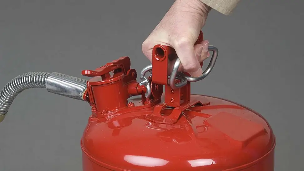 A hand grasps the handle of a Justrite gas can.