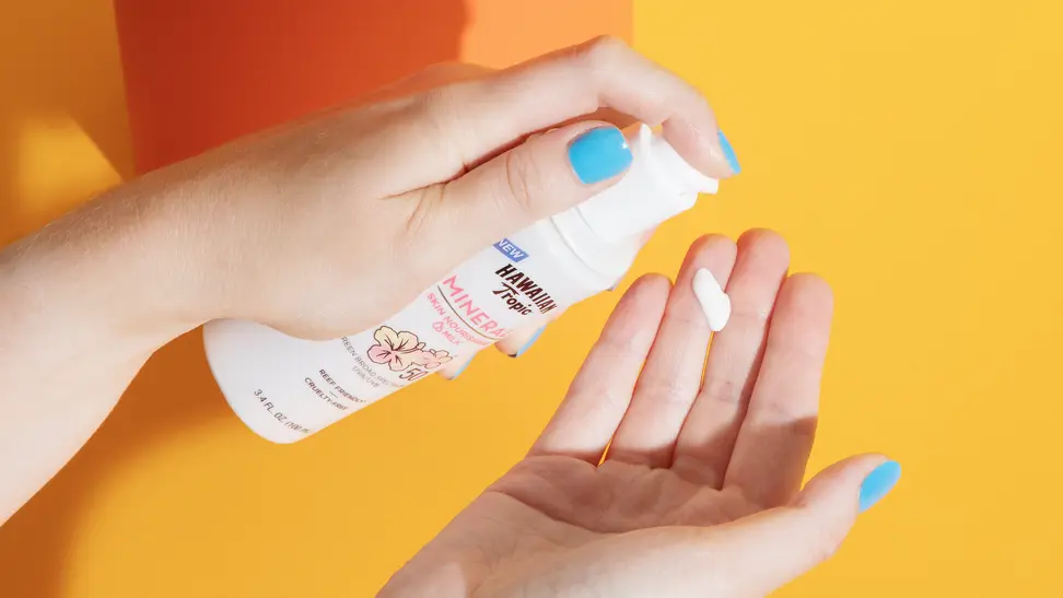 Hawaiian Tropic Milk Sunscreen poured on a woman's hands against a yellow background.