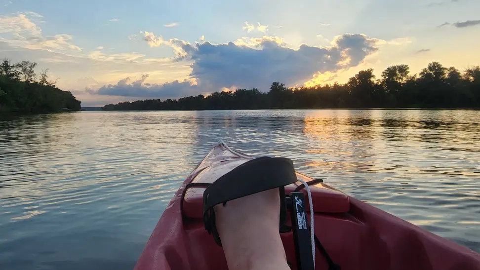 POV from seat of pedal kayak on a Missouri lake at dusk. Trees line the horizon.
