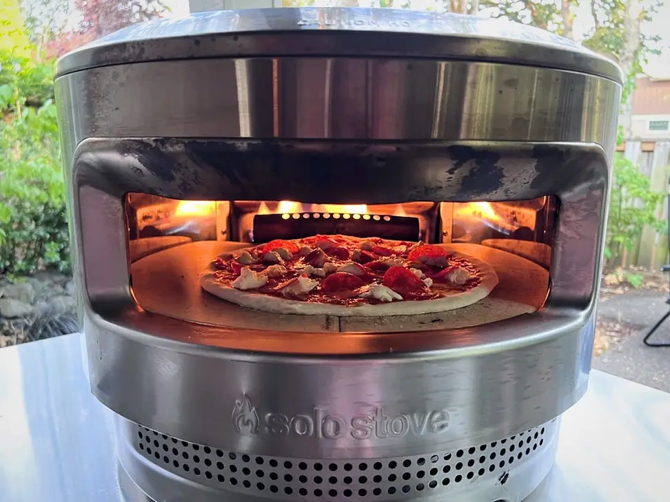 The Solo Pi sits on a counter outside. There's fire in the back of the oven and a pizza inside.