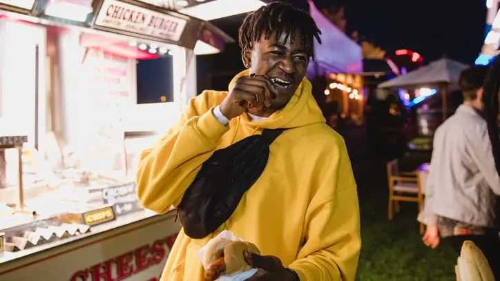 person wearing a yellow sweatshirt and black fanny pack holding a hot dog