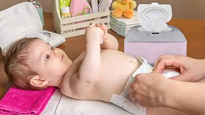 A baby's diaper being changed by her mom who is using the baby wipe dispenser and warmer.