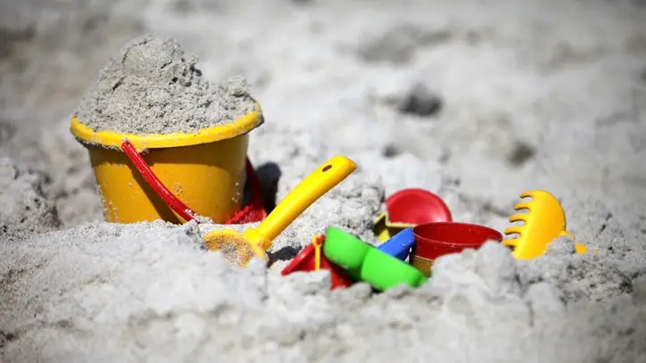 Colorful buckets, shovels, and other toys lie half-buried in beach sand.