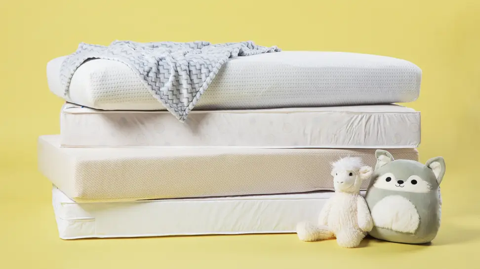 A stack of crib mattresses on a yellow background with two stuffed animals sitting on the floor next to them.