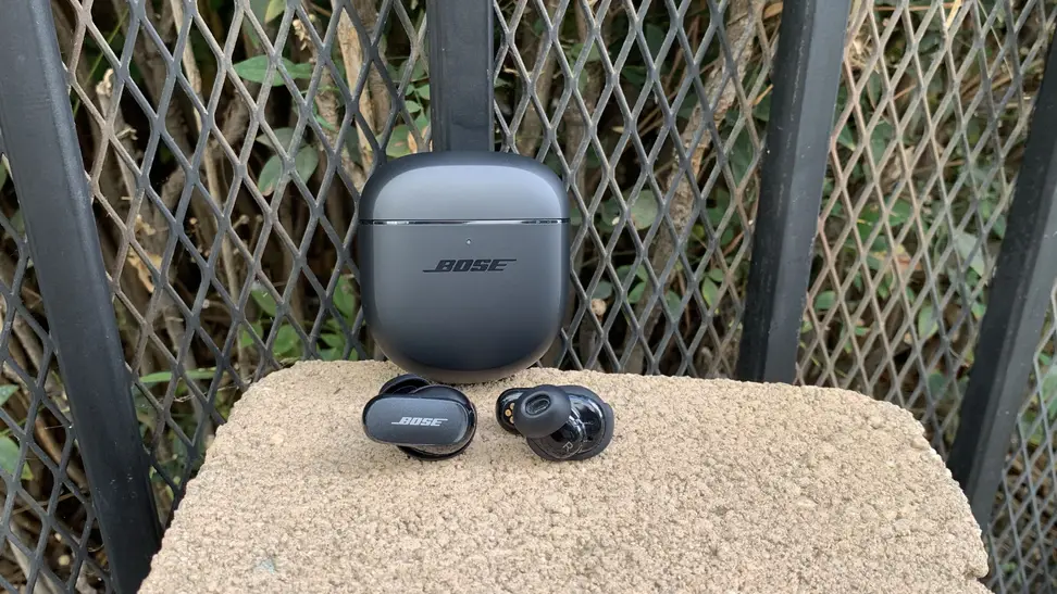 The Bose QuietComfort II earbuds with the carrying case on display in an outdoor setting.
