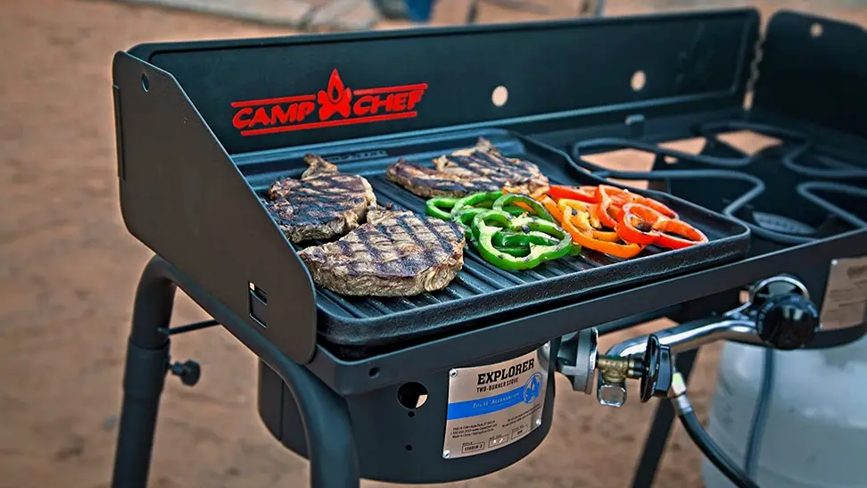 Protein and green and red peppers cook on a black Camp Chef portable grill.