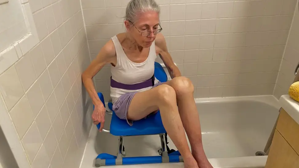 On left, elderly woman sitting in shower chair. On right, shower chair.