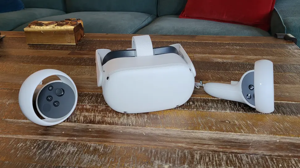 The Meta Quest 2 and its controllers sitting on a wooden coffee table with a couch and puzzle box in the background.