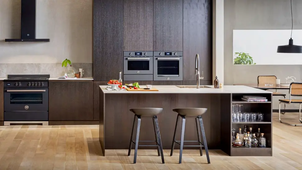 A lovely earthtone-themed kitchen with hardwood floors. There is a kitchen island, a hanging lamp, and a Bosch wall oven along the far wall.