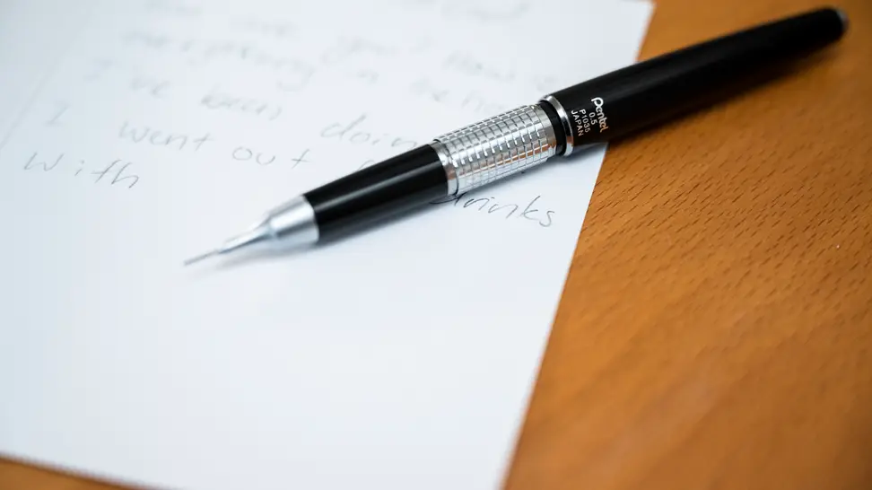 Close-up of a silver and black mechanical pencil on a desktop, along with a handwritten page of notes.