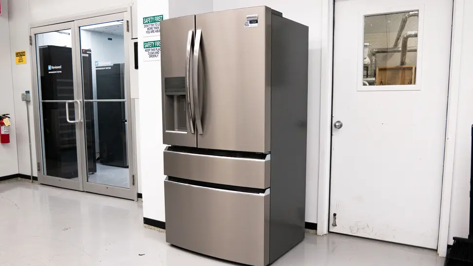 A silver French-door refrigerator stands in a lab setting against a white wall